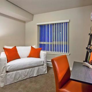 A cozy living area featuring a white couch with orange pillows, a stylish desk, and vertical blinds letting in natural light.