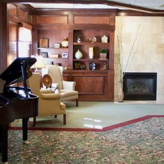 A cozy living room featuring a grand piano, a fireplace, and elegant armchairs.