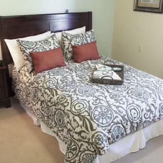 A cozy bedroom featuring a neatly made bed with patterned bedding and decorative pillows, accompanied by a wooden nightstand.