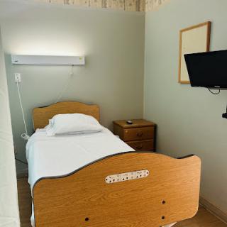A simple hospital room featuring a single bed, a nightstand, and a wall-mounted TV.