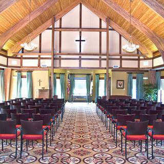 An interior view of a chapel with symmetrical seating and a wooden ceiling.
