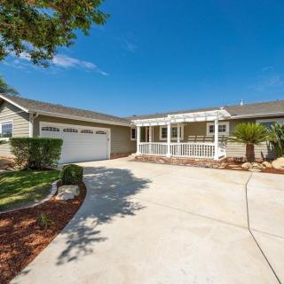 A view of a single-story house with a driveway leading to a garage, surrounded by well-maintained landscaping.