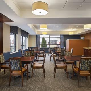 A modern dining area with neatly arranged tables and chairs, well-lit by ceiling fixtures, featuring large windows.