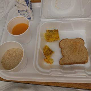 A simple breakfast tray featuring toast, oatmeal, pickles, and fruit juice.