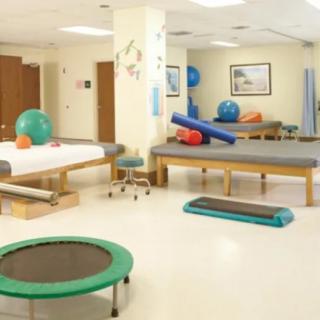 A spacious physical therapy room equipped with exercise mats, therapy tables, and various fitness equipment.