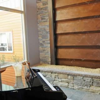 A stylish interior featuring a grand piano beside a stone and wood wall, showcasing modern architectural design.