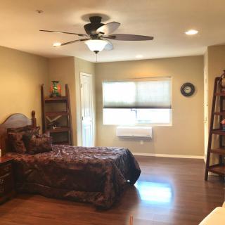 A cozy bedroom featuring a single bed, wooden furniture, and a ceiling fan, with natural light from a window.