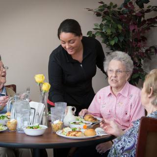 A group of elderly people enjoying a meal together with a server attending to them.