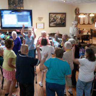 A group of seniors enjoying a gathering indoors, with a television in the background.