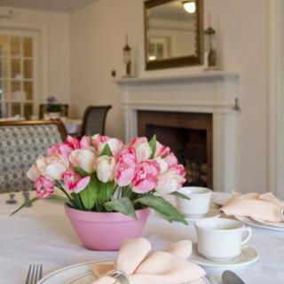 A beautifully set dining table with pink tulips and tea cups in an elegant room featuring a fireplace.