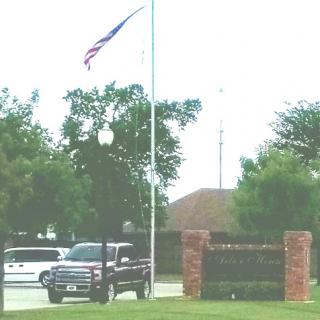 A vehicle parked near an entrance with a flag flying at half-mast, surrounded by greenery.
