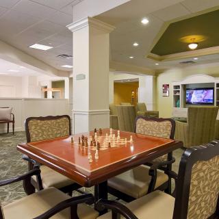 A cozy game room featuring a chess board on a table, surrounded by comfortable chairs and a TV in the background.