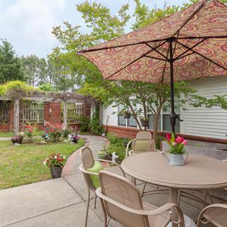 A cozy backyard patio with a table and umbrella, surrounded by greenery and potted plants.