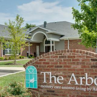 A brick building with a sign for 'The Arbor' surrounded by trees.