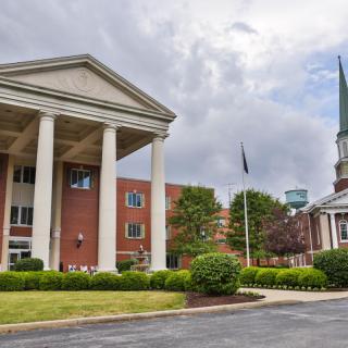 A grand building with large columns and an adjacent church featuring a steeple under a cloudy sky.