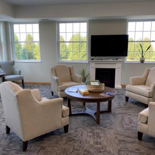 A cozy living room with armchairs, a coffee table, and a television set above a fireplace.