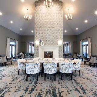 A spacious and elegantly designed dining room featuring a central fireplace, patterned carpet, and modern chandeliers.