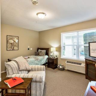 A cozy bedroom with a bed, chair, lamp, and TV by the window.