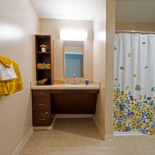 A bathroom with a wooden vanity, mirror, and decorative shower curtain featuring floral patterns. Yellow towels add a pop of color to the neutral-toned space.