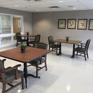 A community room with tables and chairs arranged neatly, decorated with small potted plants.
