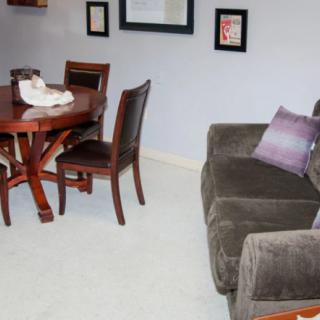 A cozy living room area with a sofa, a dining table with chairs, and framed artwork on the walls.