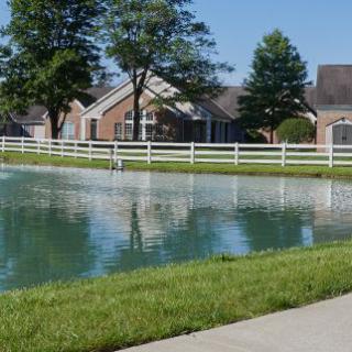 A serene residential area featuring a tranquil pond with houses and trees in the background.