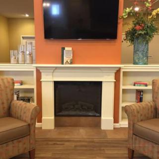 A cozy living room with a fireplace, two armchairs, and a television above the mantel.