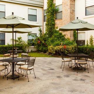 A serene outdoor patio with tables, chairs, and umbrellas surrounded by greenery.