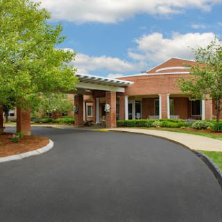 A welcoming entrance to a brick building surrounded by lush greenery on a clear day.