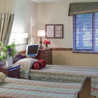 A cozy bedroom with two neatly made beds, a desk with a lamp, and flowers by the window.