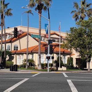 A building at a street intersection with palm trees and traffic lights on a sunny day.