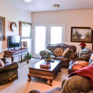 A cozy living room featuring leather sofas, a wooden coffee table, and a television, accented by framed paintings and plush cushions.