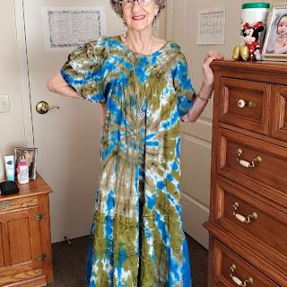 A woman poses in a vibrant tie-dye outfit, showcasing a unique fashion style in her home.