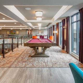 A modern game room featuring a stylish pool table with purple felt, surrounded by large windows and contemporary lighting.