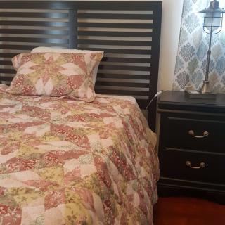A cozy bedroom with a patterned quilt and matching pillow, featuring a dark wooden headboard and a nightstand with a lamp.