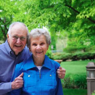 An elderly couple smiling happily in a lush, green park.