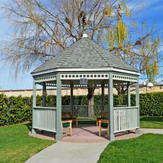 A charming wooden gazebo surrounded by a lush garden on a sunny day.