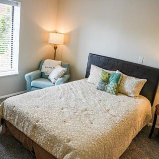 A cozy bedroom with a bed, pillows, a chair, and a lamp by the window.