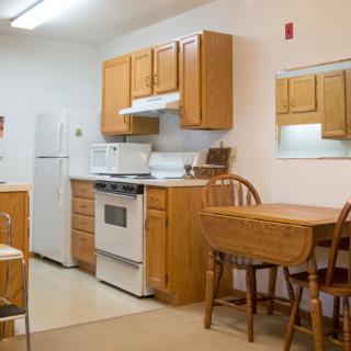 A cozy kitchen with wooden cabinets, equipped with a refrigerator, stove, and a dining table with chairs.