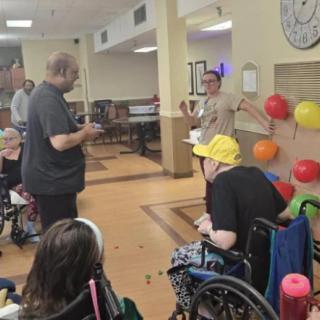 Residents in wheelchairs enjoy a group activity in a nursing home, with colorful balloons displayed on the wall.