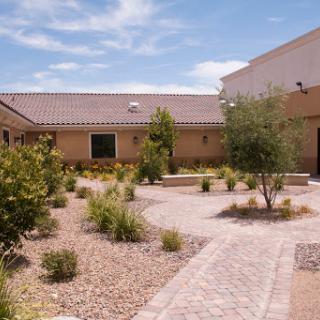 A serene outdoor pathway leads through a landscaped garden with a residential building in the background.