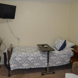 A hospital room with a single bed, wall-mounted television, and medical overbed table.