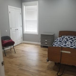 A simple bedroom with a bed, chair, and dresser on a wooden floor.