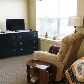 A cozy living room with a comfortable reclining chair, television on a cabinet, and a window letting in natural light.