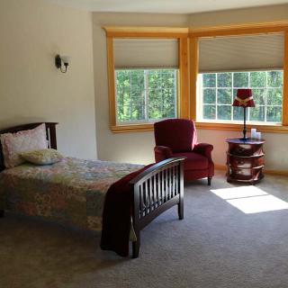 A cozy bedroom with a single bed and an armchair by the window, illuminated by natural light.