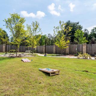 A grassy backyard with a cornhole game set up on a sunny day.