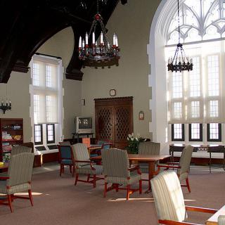 A cozy library reading room with high ceilings, arched windows, chandeliers, and comfortable seating.