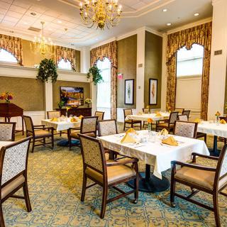 An elegant dining room with neatly arranged tables and chairs, featuring a chandelier and decorative elements.