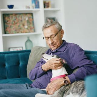An elderly man enjoys a tender moment with his dog on a cozy couch.