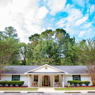 A suburban house with a front porch and surrounded by trees under a partly cloudy sky.